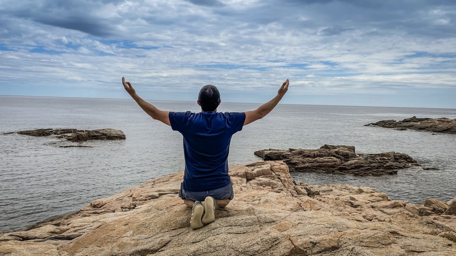 a man sitting on top of a rock near the ocean