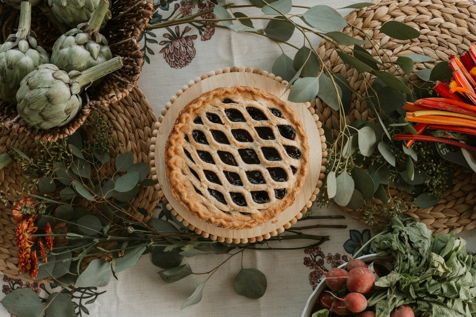 A lattice-top pie surrounded by autumn harvest vegetables and greenery.